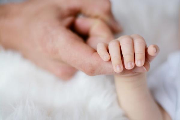 La mano di un neonato stringe il dito di un adulto.